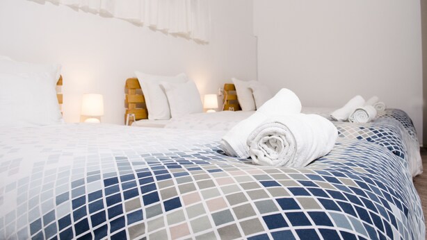 A hotel room with a neatly made bed, a bedside lamp, and a window with sheer curtains. - Villa Re3Ca (Skopje)