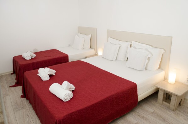 Une chambre d’hôtel avec deux lits, chacun recouvert d’une couverture rouge et doté d’oreillers blancs, ainsi qu’une petite table de chevet avec une lampe.