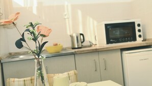 A kitchen with a microwave, kettle, and a vase with flowers on the counter. - Villa Re3Ca (Skopje)