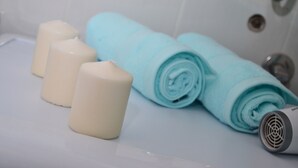 A bathroom with a bathtub, white candles, a rolled-up towel, and a hairdryer. - Villa Re3Ca (Skopje)