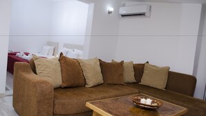 A brown sofa with beige cushions, a wooden coffee table with a candle holder, and a bed with white linens in the background. - Villa Re3Ca (Skopje)