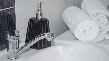 A bathroom with a chrome faucet, a black soap dispenser, and neatly rolled white towels.