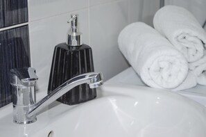 A bathroom with a chrome faucet, a black soap dispenser, and neatly rolled white towels. - Villa Re3Ca (Skopje)