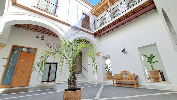 Un pati amb una banca de fusta, plantes en testos i una escala que mena a un nivell superior.