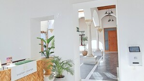 Una zona d'entrada amb un taulell de recepció de fusta en patrons de petxina, una planta en test i un llum modern amb diverses làmines esfèriques.