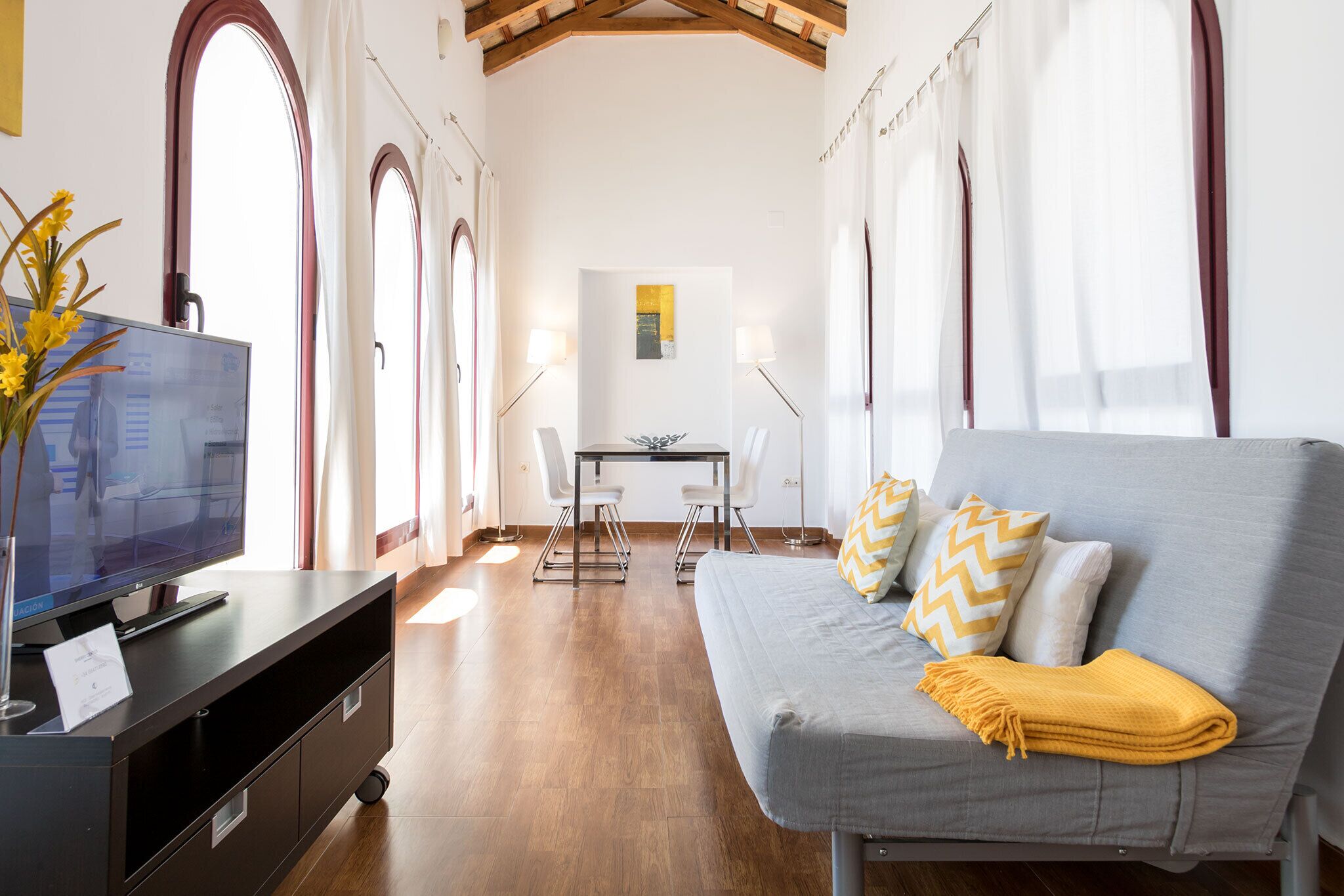 Un soggiorno moderno con un divano grigio, una TV su un mobile nero e un'area pranzo con tavolo e sedie.