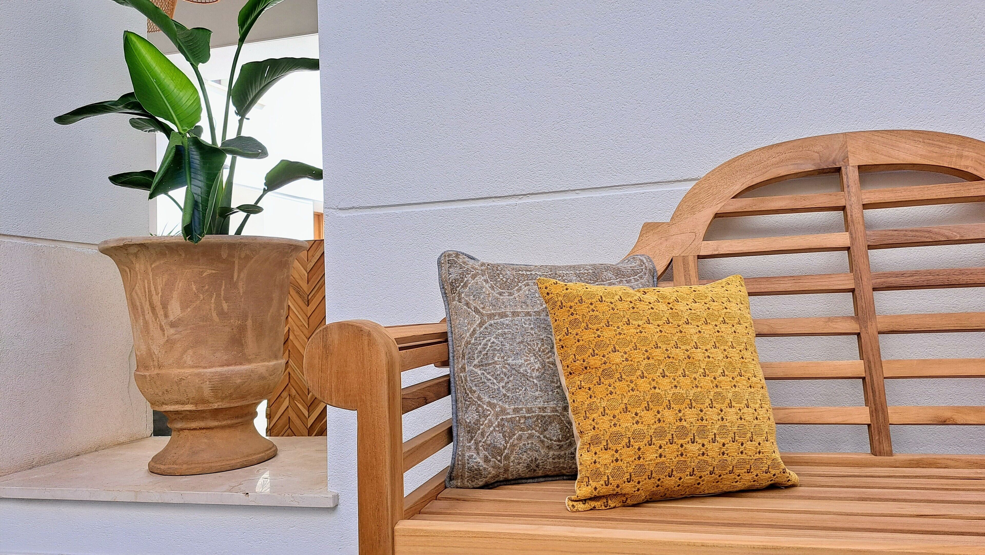 Una planta en maceta y dos almohadones sobre un banco de madera.
