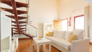 Un saló modern amb escala de fusta, sofà blanc i taula petita blanca.