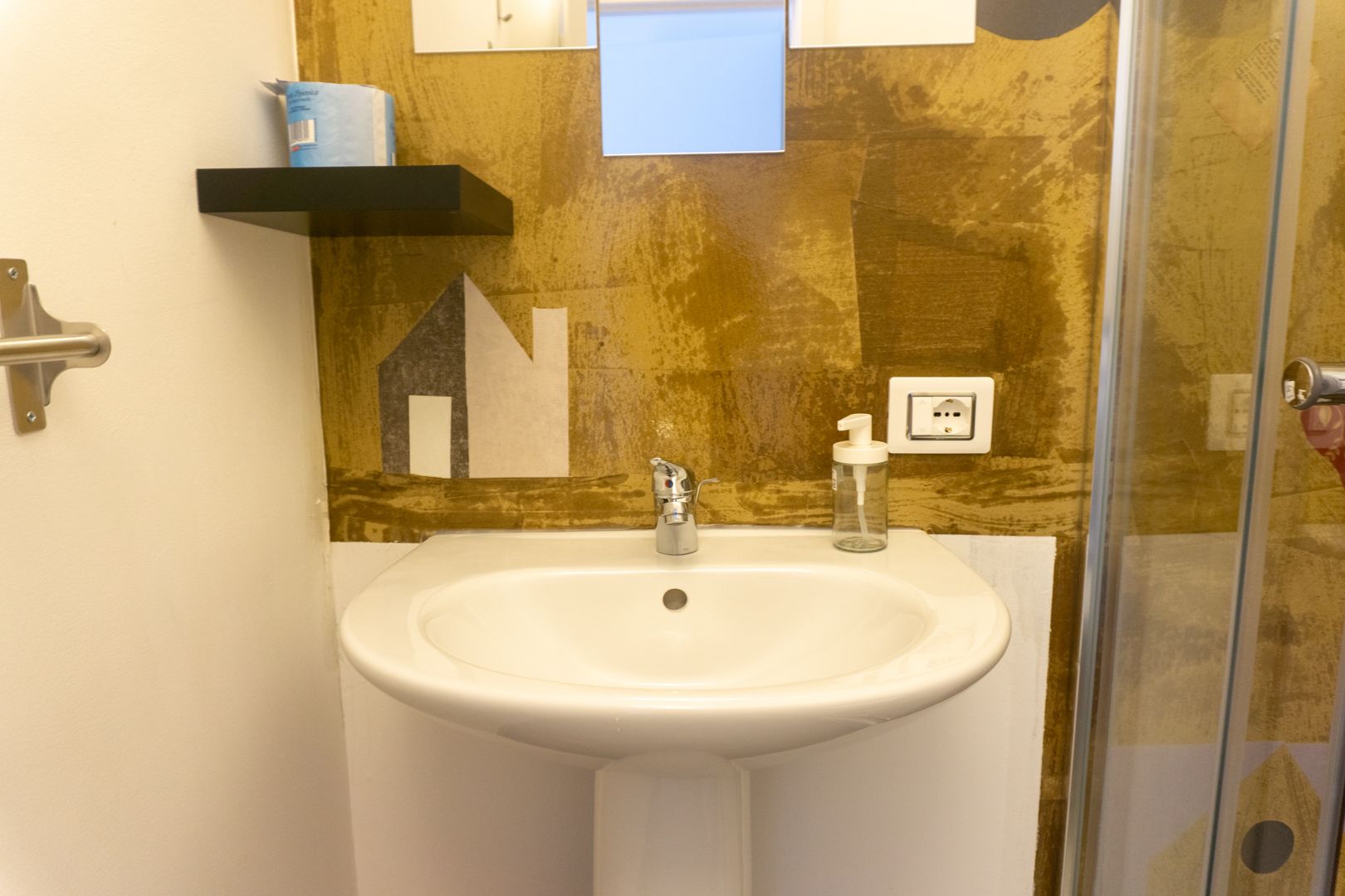 A bathroom with a white sink, a mirror, a soap dispenser, and a shelf with a blue container.