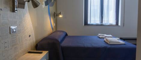 A bedroom with a bed, a desk, a lamp, and a window with curtains.