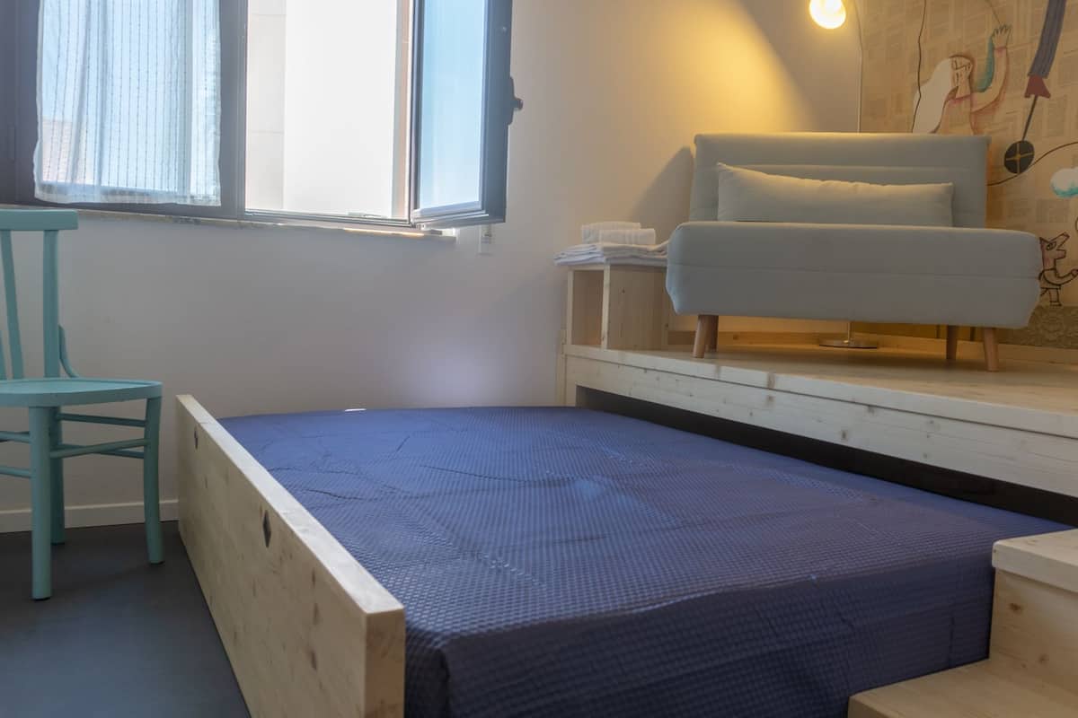 Pieni, pelkistetty huone, jossa on yksi sänky, tuoli ja sohva.