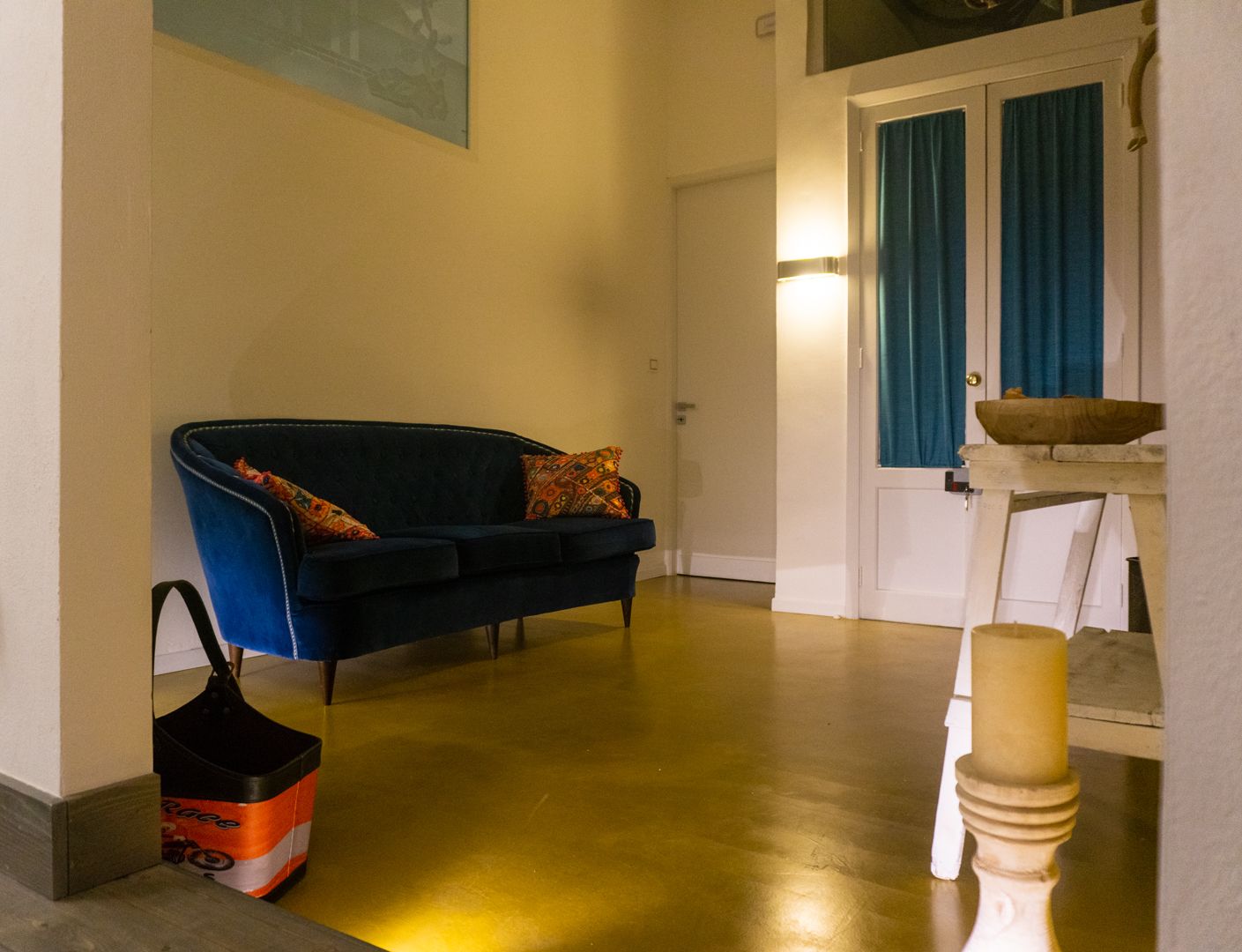 A hallway with a blue sofa, a white table with a bowl, and a wooden floor.