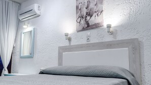 Un dormitorio con pared blanca texturizada, aire acondicionado instalado, un cuadro con caballos y una cama con colcha gris.