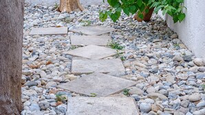 Un sendero de piedra que conduce a una pared blanca, rodeado de guijarros y un tocón de árbol.
