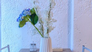 Una mesa de comedor con un florero blanco, dos sillas y una pared con textura.