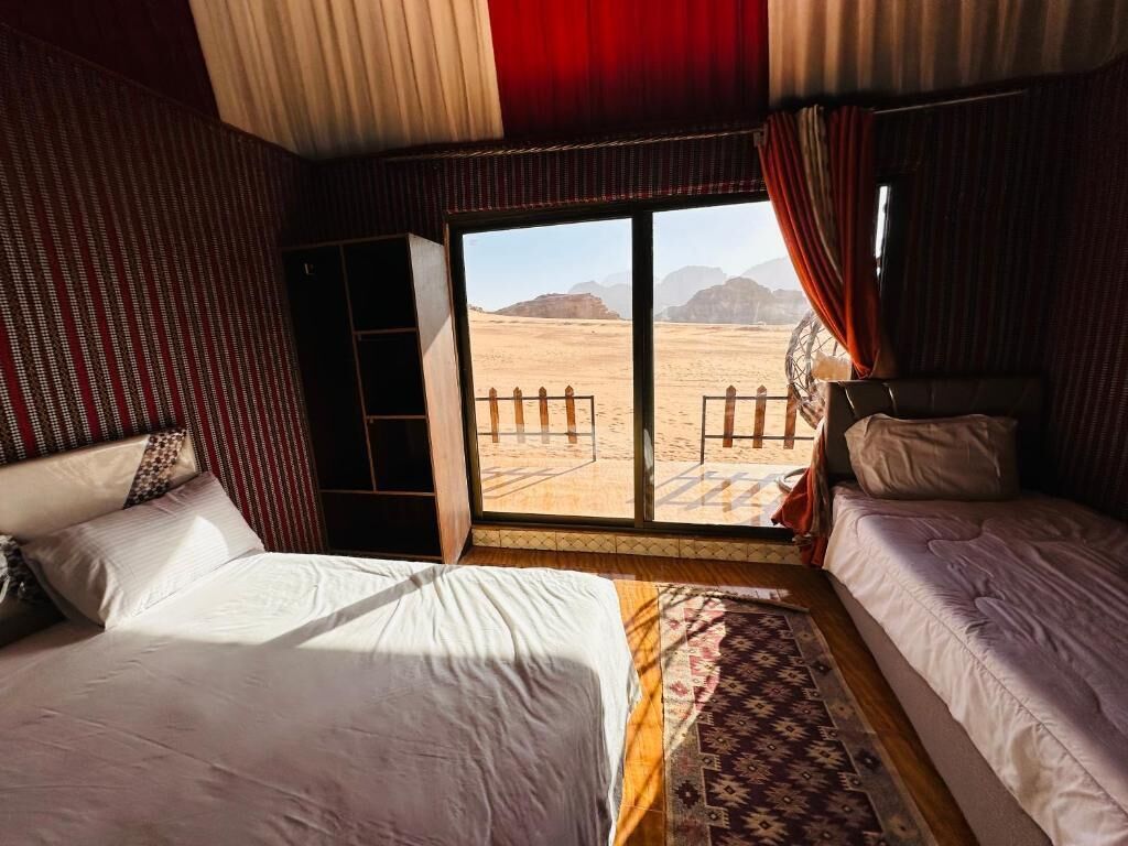 A room with two beds, a large window with a view of a desert landscape, and a patterned rug.