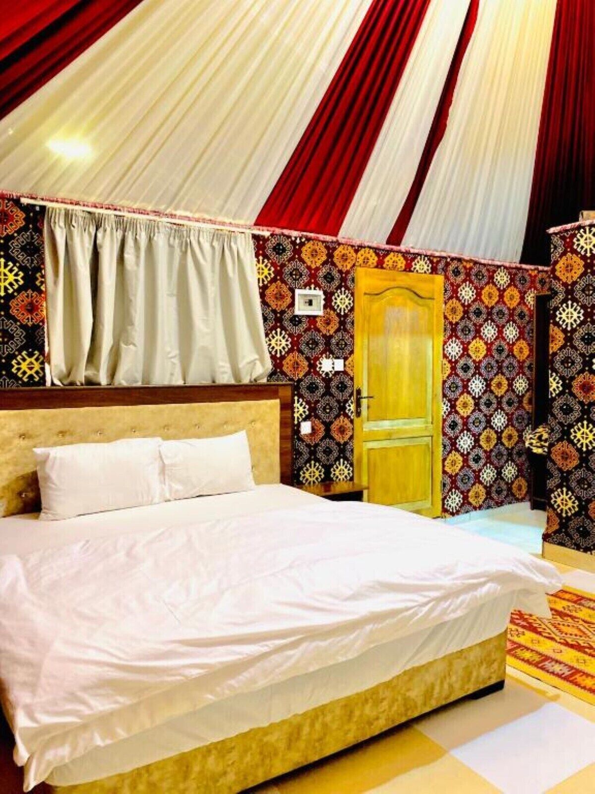 A room with a bed, curtains, patterned walls, and a door.