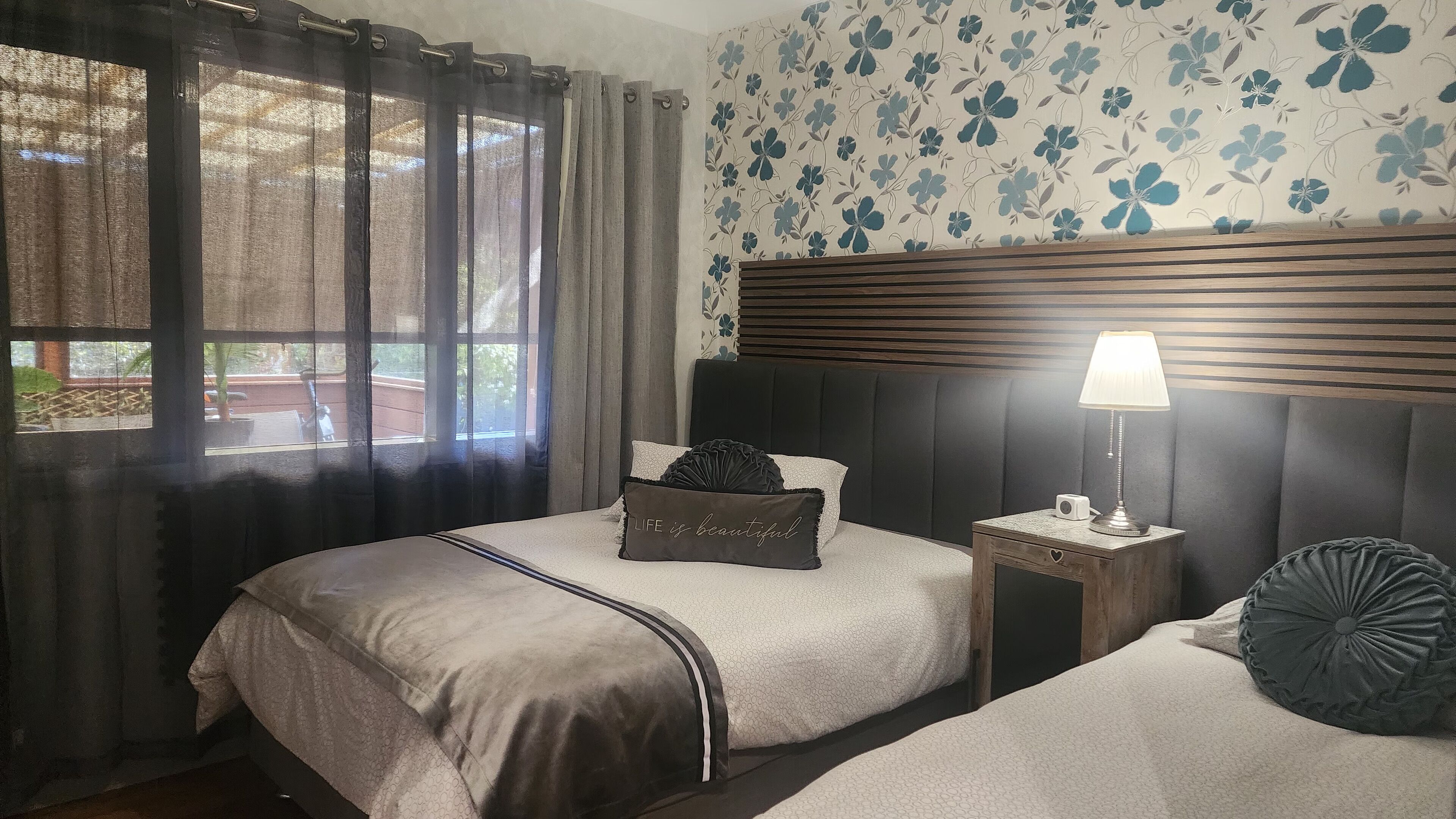Une chambre avec deux lits, une table de chevet avec une lampe et une fenêtre avec des rideaux.