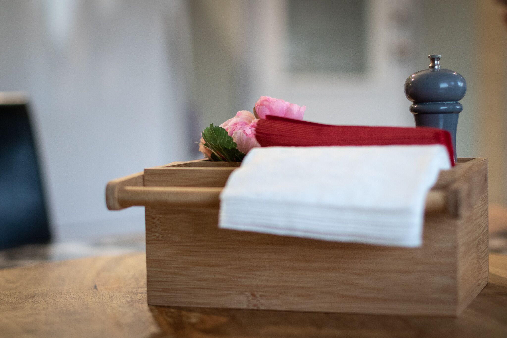 A wooden chest with a white cloth and a red cloth on top, a pink flower, and a pepper grinder.