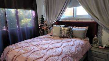 A bedroom with a bed, a nightstand, a window with curtains, and a floral wall pattern.