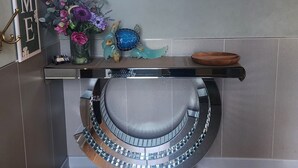 Un baño moderno con un espejo grande, un letrero de bienvenida, un florero decorativo y suelo de madera.