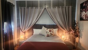 Una cama bien hecha con cabecera, dos mesitas de noche con lámparas y un ventanal con cortinas.
