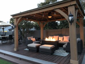 An outdoor patio with a wooden pergola, wicker furniture, a fire pit, and a dining area with an umbrella. - Resort style house centrally located w/ Zen backyard and putting green (San Diego)