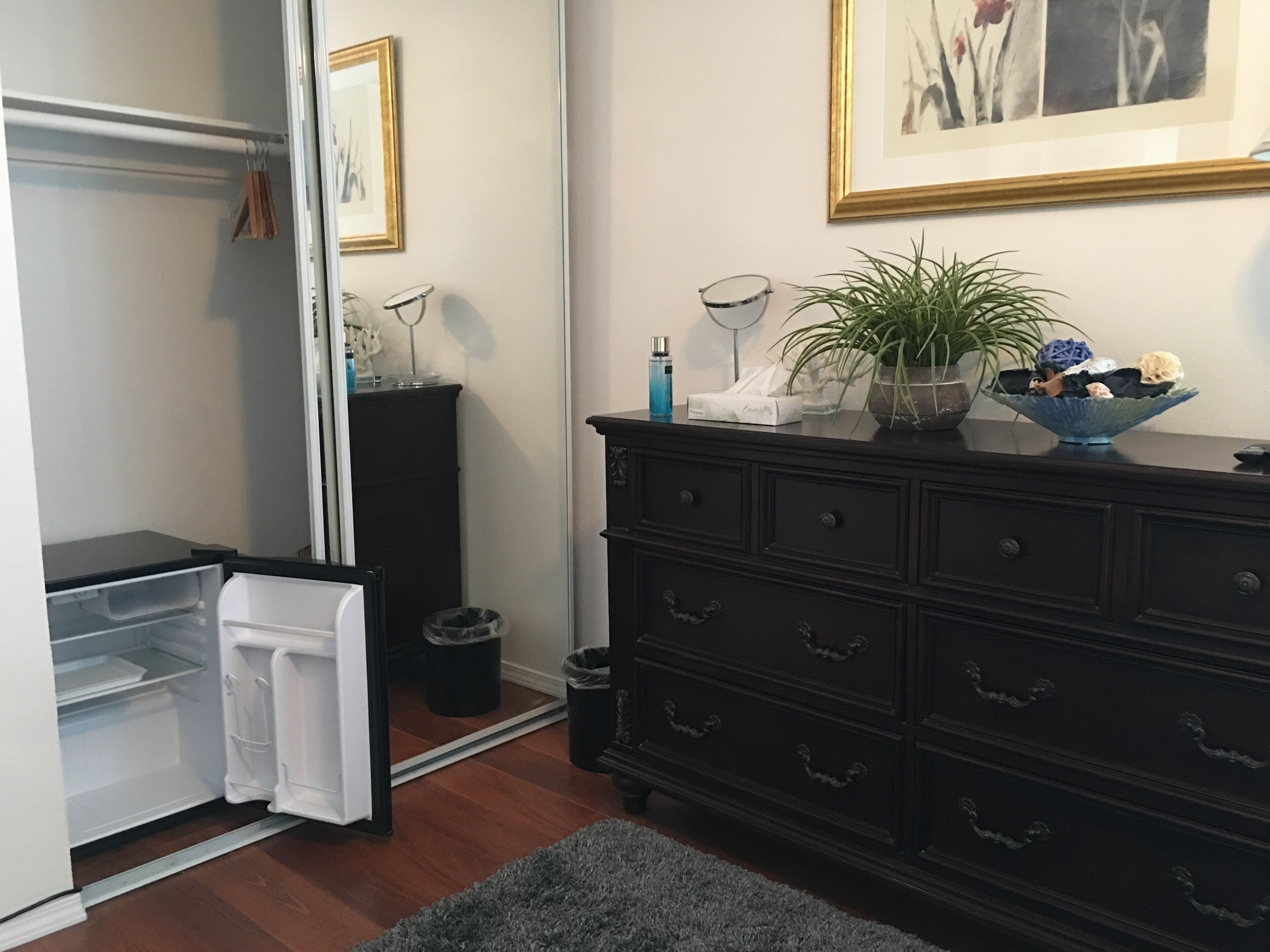 A compact kitchen with a refrigerator, a dark wooden dresser, and a mirror.