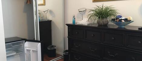 A compact kitchen with a refrigerator, a dark wooden dresser, and a mirror.