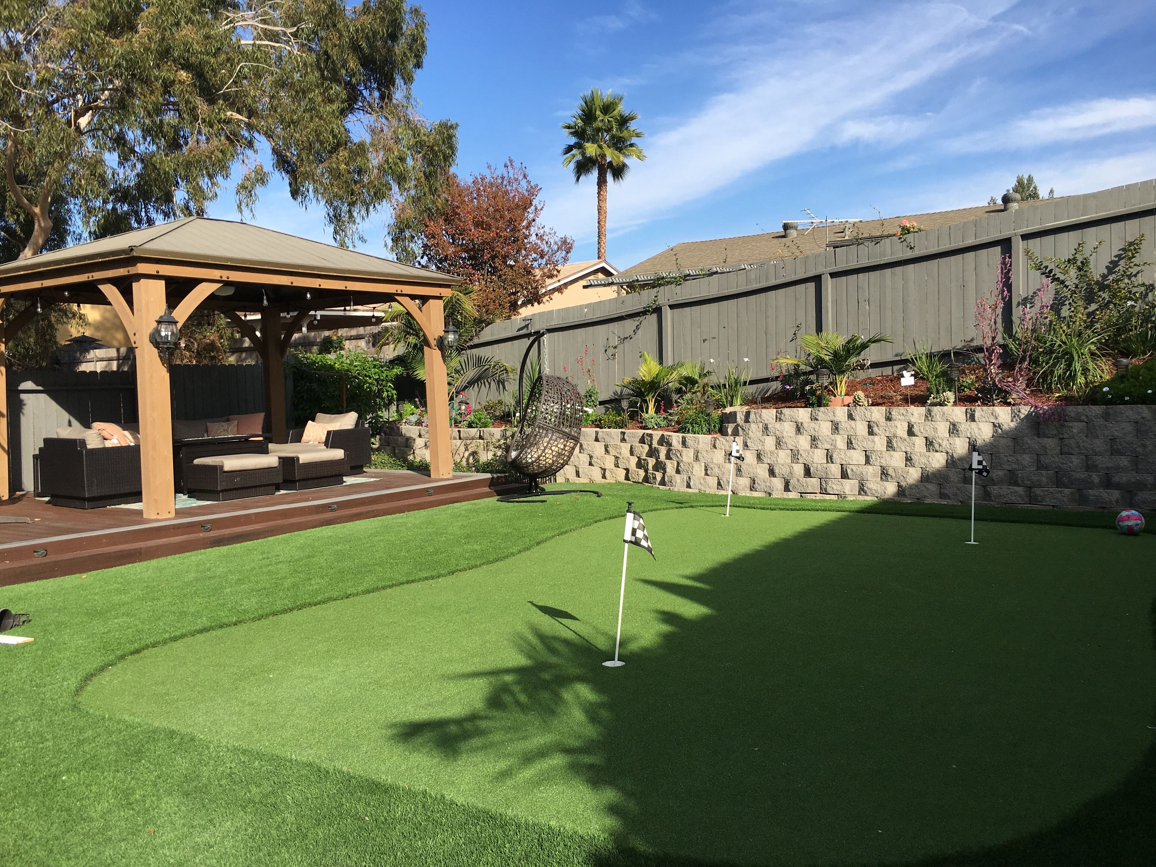 A backyard with a wooden pergola, artificial grass, and a stone wall.