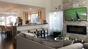 Een moderne woonkamer met een grote bank, een keuken met een bar, en een televisie waarop een golfwedstrijd wordt vertoond.