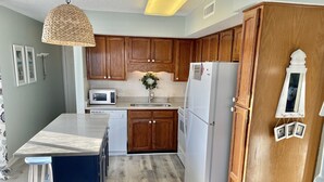 Une cuisine moderne avec des meubles en bois, un réfrigérateur blanc, un four à micro-ondes et un grand îlot central doté de tabourets de bar.