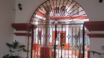 An arched metal gate with intricate designs, leading to an outdoor area with a tiled floor and potted plants.