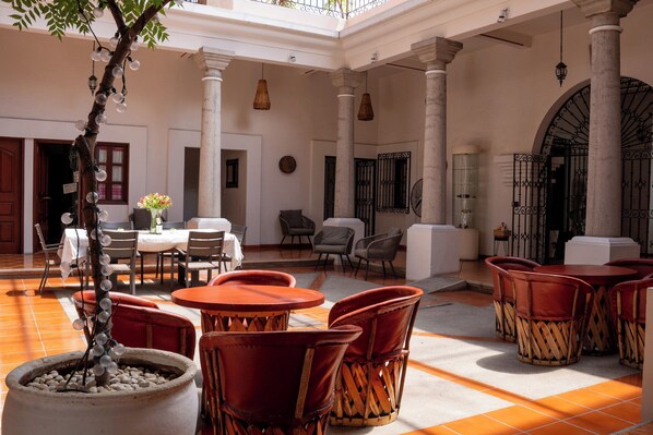 A spacious courtyard with a central tree, multiple seating areas, and a large arched entrance.