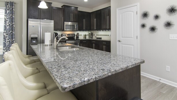 A modern kitchen with dark cabinets, a granite countertop, a stainless steel refrigerator, and a microwave. - ~BEAUTIFUL HOME NESTLED IN THE PERFECT TOWN~ (Bluffton)