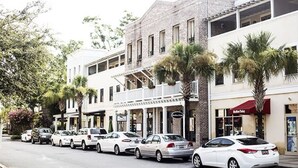 A street lined with white buildings, some with balconies and storefronts, parked cars, and palm trees. - ~BEAUTIFUL HOME NESTLED IN THE PERFECT TOWN~ (Bluffton)