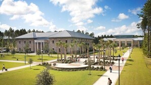 A large building with a central courtyard, surrounded by palm trees and a well-maintained lawn. - ~BEAUTIFUL HOME NESTLED IN THE PERFECT TOWN~ (Bluffton)