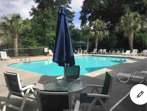 Relax by the serene pool surrounded by lush greenery and lounge chairs.