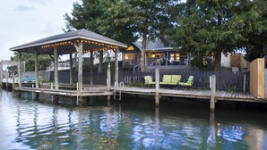 Ein an einem Steg festgemachtes Boot mit überdachter Sitzgelegenheit und Stühlen, einem Holzzaun und einem Haus im Hintergrund.