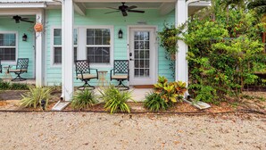 A two-story building with a green exterior and a covered porch with two chairs and a small table.