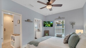 A bedroom with a bed, a ceiling fan, a TV, and a window with blinds.