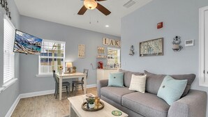 A living room with a gray sofa, a wooden coffee table, a dining area with a white table and chairs, and a ceiling fan.
