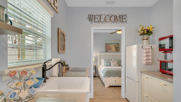 A compact kitchen with a sink, a refrigerator, and a dining area. A welcome sign is displayed on the wall.