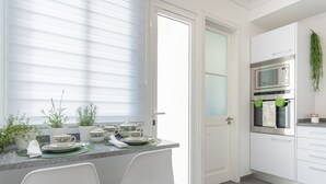 A modern kitchen with white cabinets, a built-in oven, and a window with blinds.