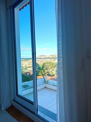 A room with a large window offering a view of a cityscape and a hill.