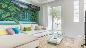 A living room with a large mural, a glass coffee table, and a beige sofa.