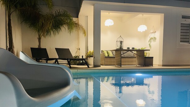 An indoor swimming pool with lounge chairs and a seating area with a table and plants.