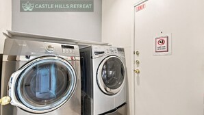 A laundry area with two front-loading washing machines and a sign indicating 'Castle Hills Retreat.' - Central, Airport & Downtown: Hotel House Retreat (San Antonio)