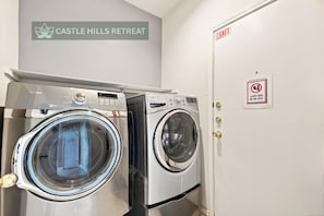A laundry area with two front-loading washing machines and a sign indicating 'Castle Hills Retreat.' - Central, Airport & Downtown: Hotel House Retreat (San Antonio)
