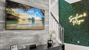 A reception desk with a large TV displaying a scenic landscape, a Wi-Fi sign, and a neon sign on the wall. - Park all day, recharge in style- 10min to Disney, clean, revamped w/ resort pool (Kissimmee)